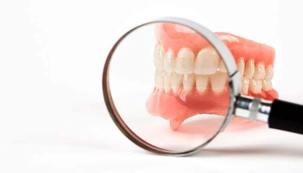 虫眼鏡で入れ歯を見ている画像