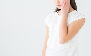 痛みを感じて頬を押さえている女性の写真