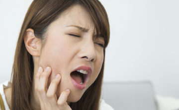 虫歯を放置した痛みで頬を押さえている女性の写真
